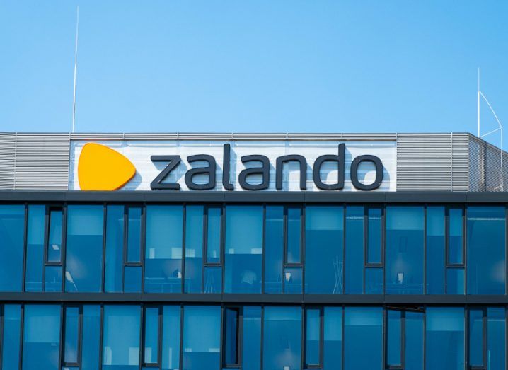 The Zalando logo on the top of a building, with windows below it and a blue sky above.