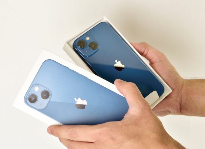 A person opening a small box that has a dark blue iPhone inside with the Apple logo on its back. The box case also has an image of the iPhone.