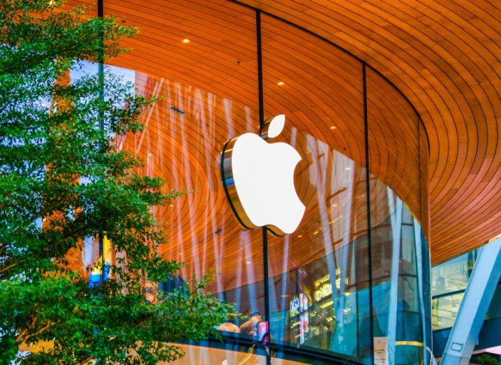 The Apple logo on the window of a building, with a wooden roof above it and a tree to the left side.