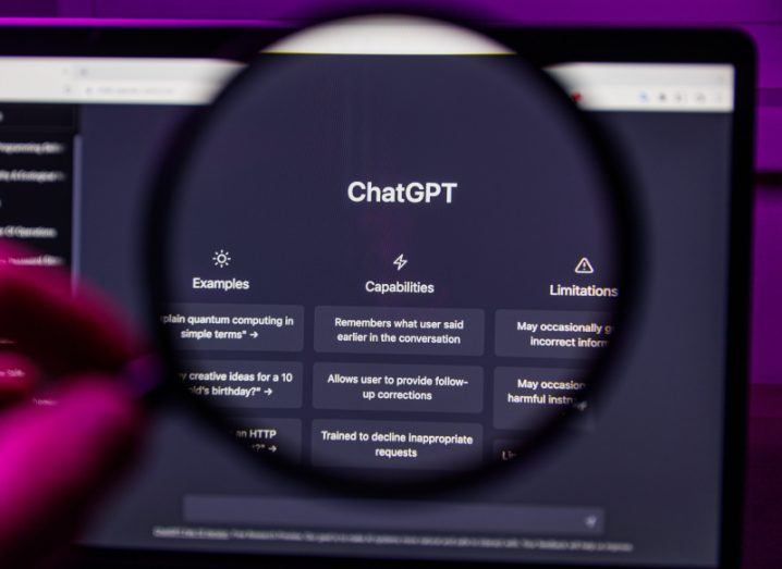 The ChatGPT logo on a laptop screen, with a person's hand holding a magnifying glass at the screen.