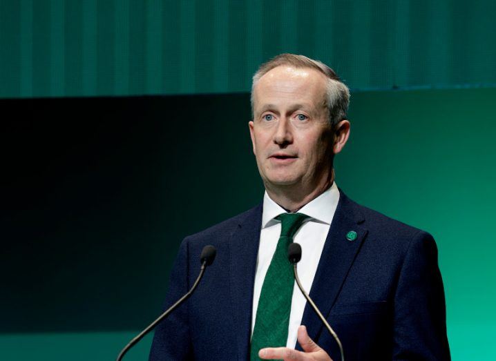 A man wearing a suit and green tie stands in front of two microphones. He is Enterprise Ireland's Leo Clancy.