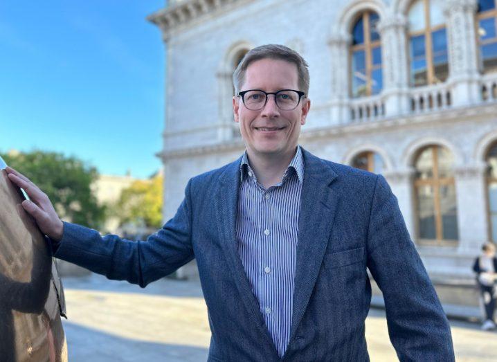 Prof Holger Claussen standing outside a building with his hand resting on a statue.