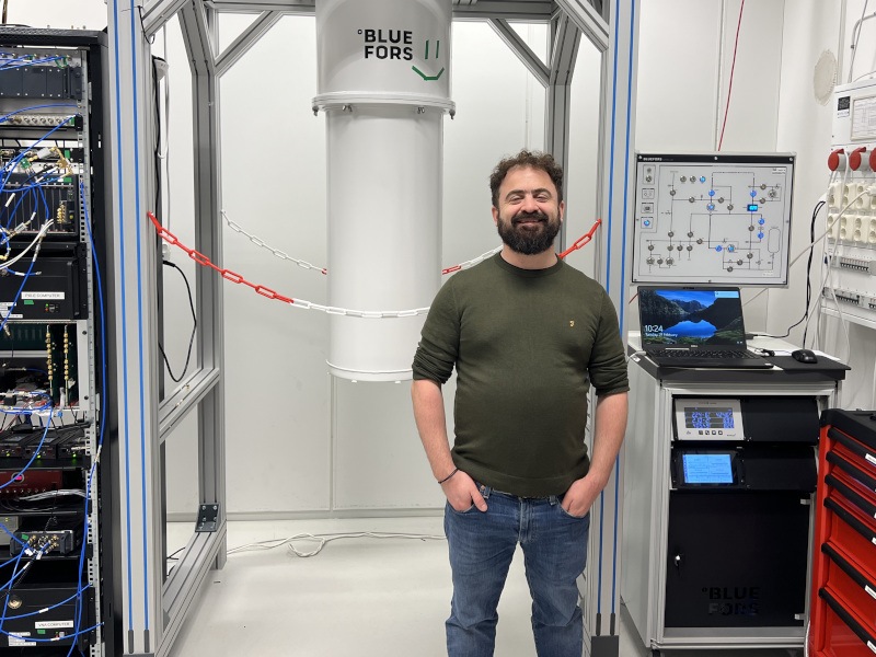 A man stands in a lab with his hands in his pockets smiling at the camera.