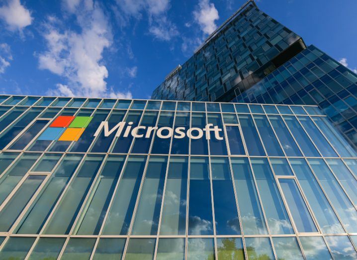 An upwards-facing shot of a large glass office against a blue sky with the Microsoft logo across the top.