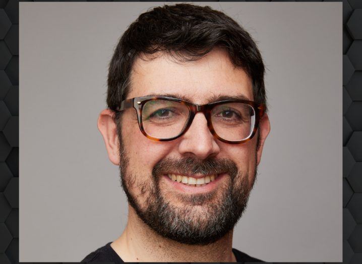 A headshot of a man with glasses and a beard smiling with a grey wall behind him. He is Paulo Rodriguez, head of international at Vanta.