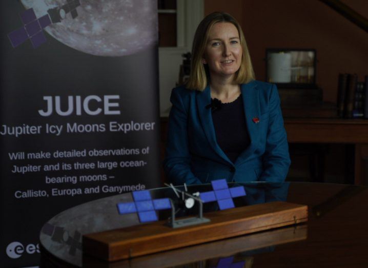 Prof Caitriona Jackman from DIAS standing at a lectern in dim light with a banner for the ESA Juice mission behind her.