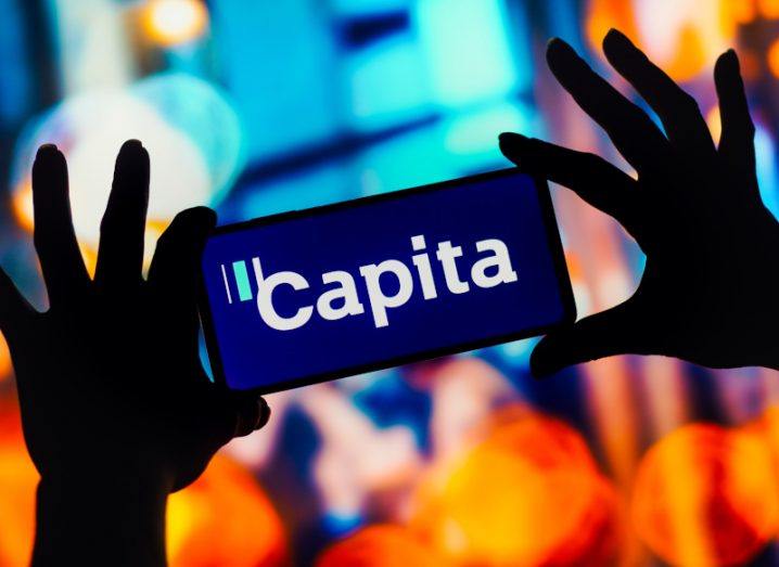 The Capita logo on a smartphone held in a person's hands.