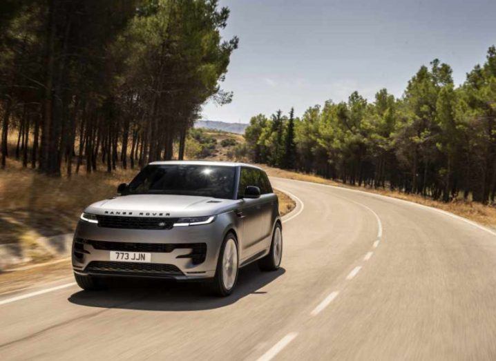 A steel-coloured Range Rover EV made by Jaguar Land Rover in motion on a road with trees on both sides.