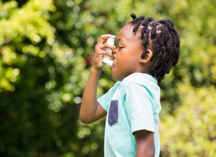 Young boy using an asthma inhaler in the outdoors.