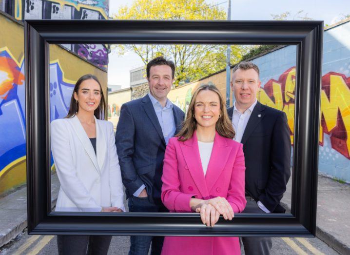 Two women and two men associated with EY Entrepreneur of the Year stand inside a physical frame in an alleyway with graffiti on the walls on either side.