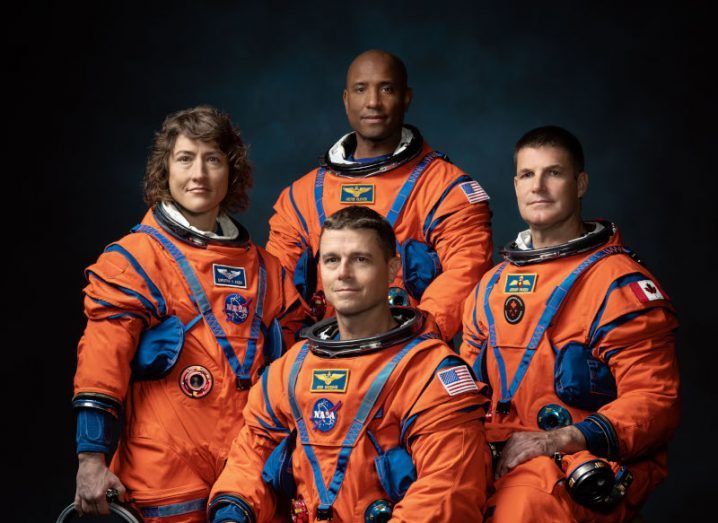 NASA Artemis II crew members wearing orange spacesuits. Photo shows four people including a woman on the left and a black man at the back.