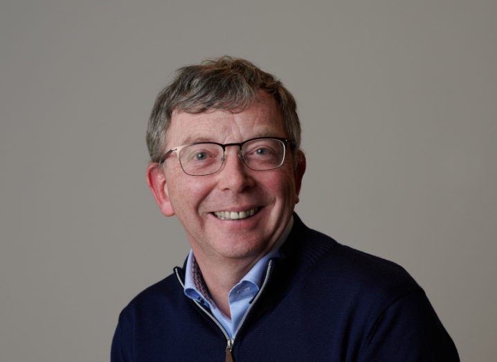 Headshot of a man in a dark blue jumper, with a light brown wall behind him. He is Alan Merriman, Elkstone CEO.