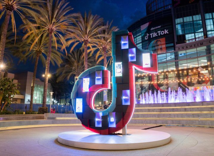 A statue of the TikTok logo in the middle of a courtyard at night, with trees and a building in the background.