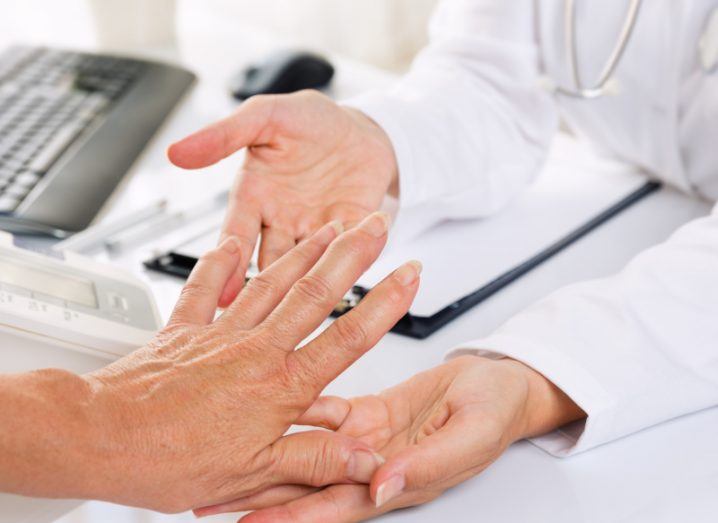 A doctor holding a person's hand over a desk. Used as a concept to show rheumatoid arthritis, an autoimmune disease.