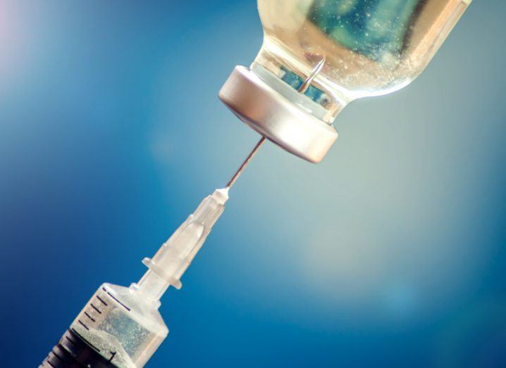 A needle injected into a vial of liquid, with a blue background.