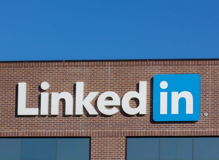 The LinkedIn logo on the front of a brown building, with a blue sky above it.