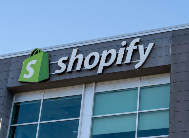 The Shopify logo on the top of a building, with windows below and a blue sky overhead.