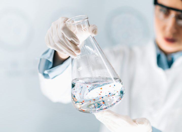 A scientist holding a glass container that contains water with small bits of coloured plastic inside it.