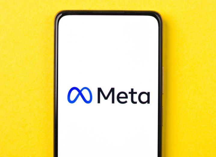 Phone with the Meta logo on it resting on a yellow background.