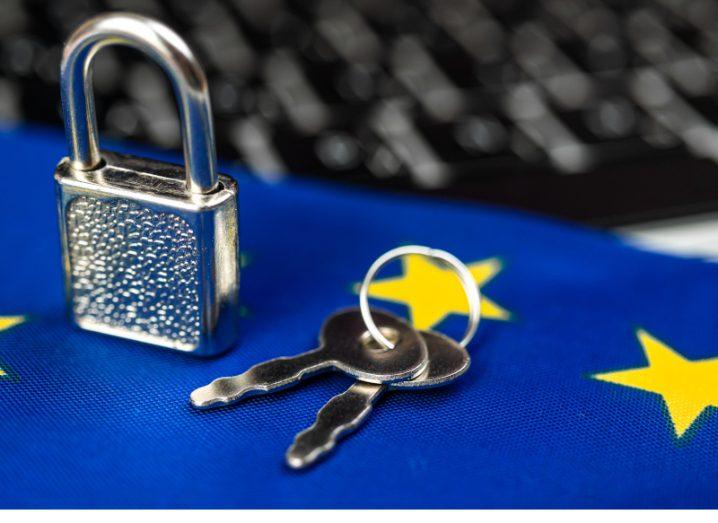 A pair of keys and a small lock on an EU flag with a computer keyboard in the background in a cybersecurity concept.