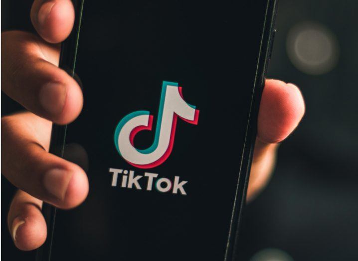 The TikTok logo on a smartphone screen, held in a person's hand.