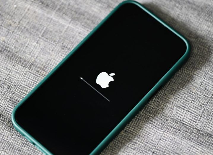 The Apple logo on a smartphone screen, with a small update line under it. The phone is laying on a grey surface.