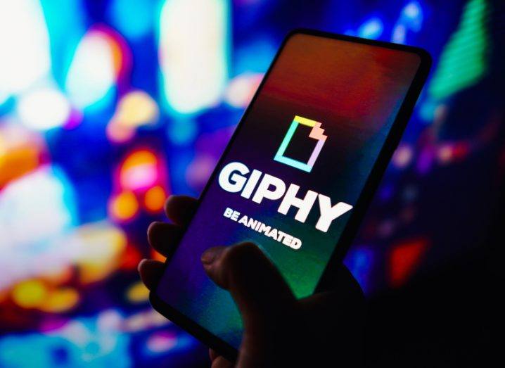 The Giphy logo on a smartphone, held in a person's hand.