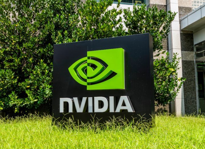 The Nvidia logo on a black square signpost in front of a building, with grass under the sign and a green bush behind it.