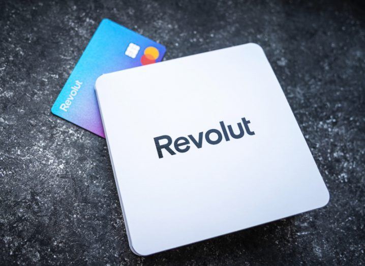 The Revolut logo on a white sticker, laying on a concrete surface with a Revolut debit card next to it.
