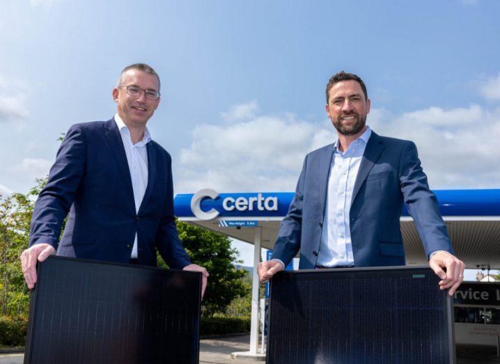 Two men standing together with a Certa logo in the background. They are holding small solar panels.