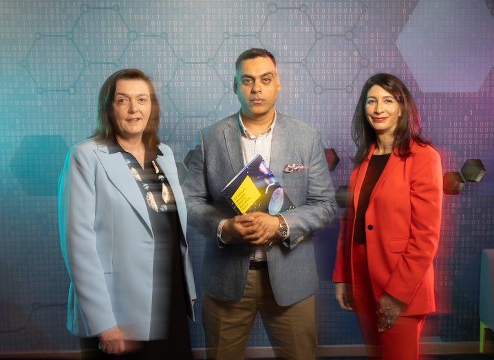 A man and two women standing together in front of a wall with zeros and ones written on it. They are employees of EY Ireland.