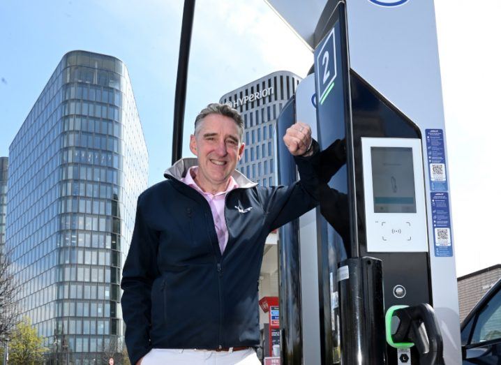 A man standing next to an electric vehicle charging station, with buildings in the background. He is Maurice Neligan, CEO of Jolt Energy.