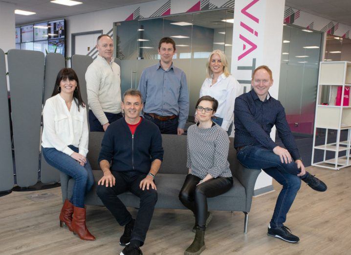 Seven people who work for Viatel gathered around a couch in an office posing for a photo.