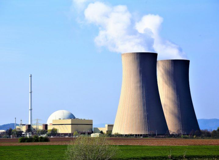 Nuclear reactors in a green field with with white smoke being released from the top.