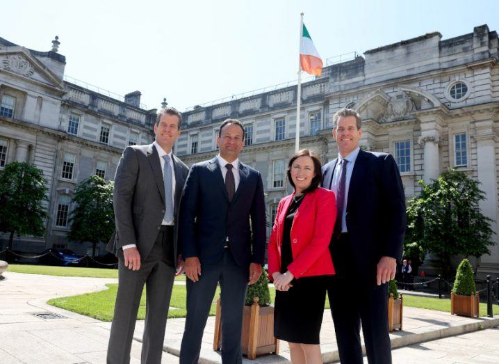 The Winklevoss twins of Gemini stand on either side of Leo Varadkar and Siobhán Hanley in a square with old buildings surrounding them.