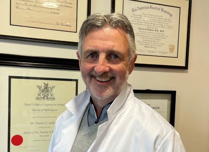 Headshot of Frank Sullivan wearing a doctor's coat and standing in front of framed certificates on a wall. He is a leading expert in clinical trials based in Ireland.