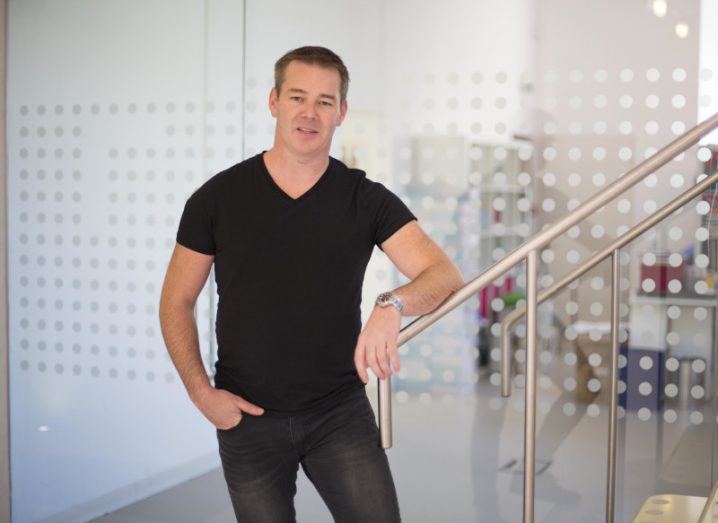 Alan Herlihy, founder and CEO of EVergreen, leans on the banister of a staircase wearing a black t-shirt and black jeans.