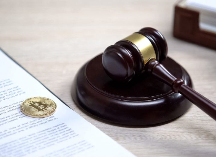 A coin with the bitcoin logo sits on a sheet of paper next to a judge's gavel, symbolising cryptocurrency regulation.
