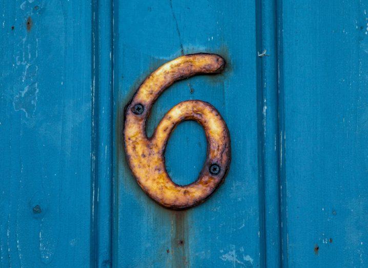 A rusty gold number six on a blue door.