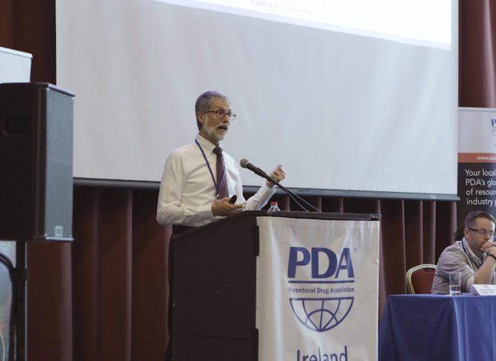 A man speaking at a podium that has the PDA Ireland chapter logo on it.