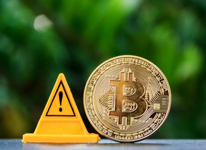 A bitcoin next to a yellow cone that has a warning symbol on it. Used to represent risk in the crypto sector.
