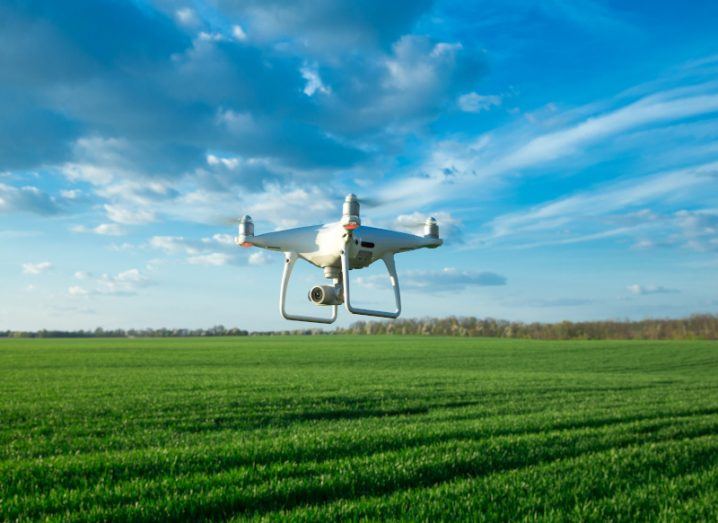 A grey drone hovering over a field, with a blue sky in the background.