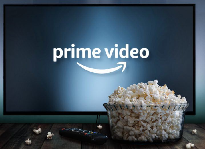 A TV with the Amazon Prime Video logo on the screen and a bowl of popcorn in front on a wooden table, next to a remote control.