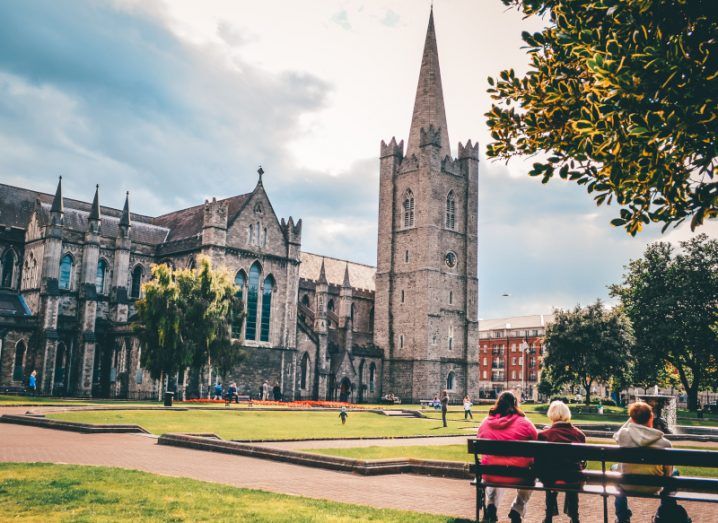 St Patrick's Cathedral Dublin with people sitting on a bench outside it in the garden.