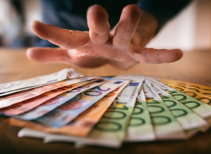 A hand reaching out for a pile of euro notes of different denominations.