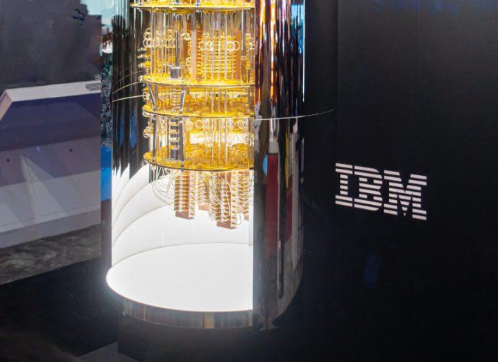 A quantum computer next to a wall with the IBM logo on it.