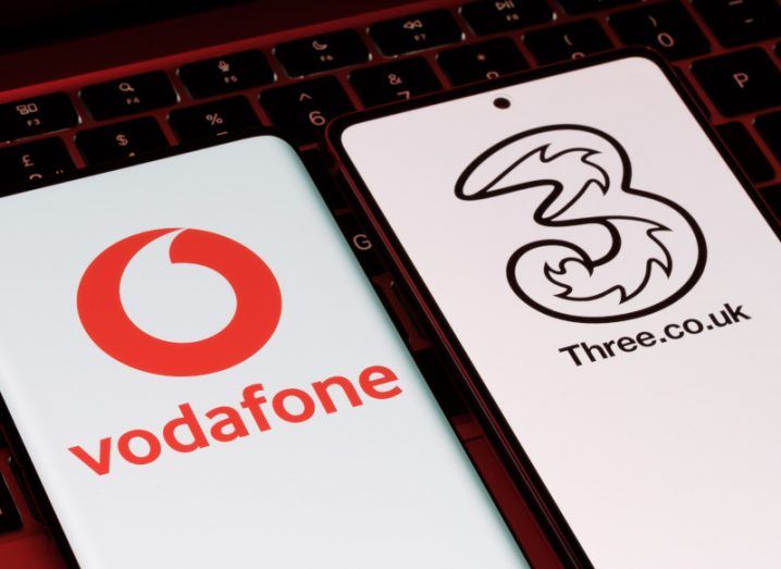 Two mobile phones with the Vodafone and Three company logos on them, laying on a computer keyboard.