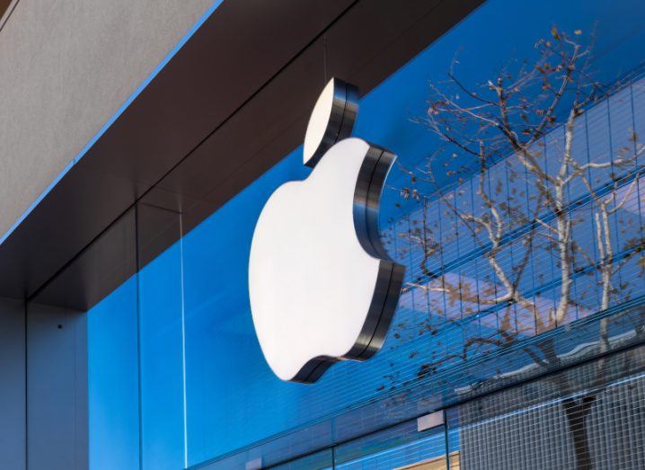 Apple logo on the front of an office with a glass front and tree branches visible.