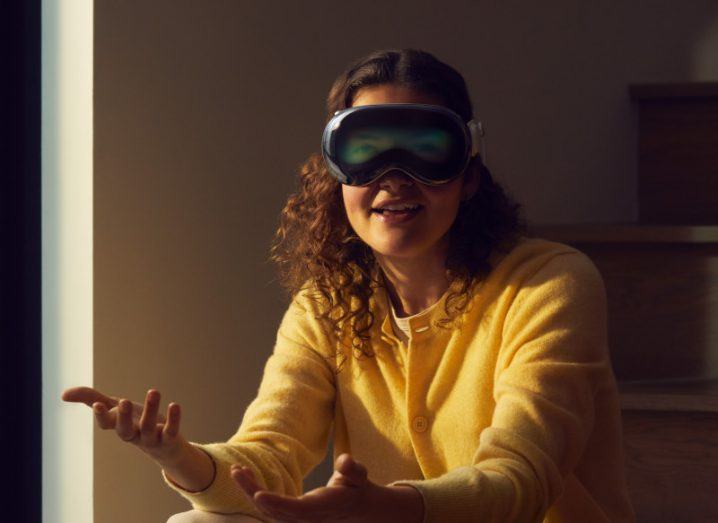 A woman sitting on some stairs wearing an Apple Vision Pro mixed reality headset.