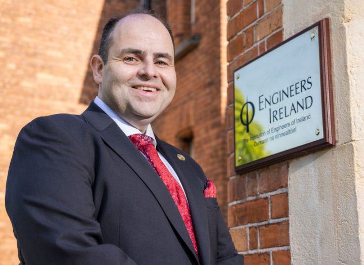 Edmond Harty president of Engineers Ireland standing outside a red brick building with a gold plaque on the door.